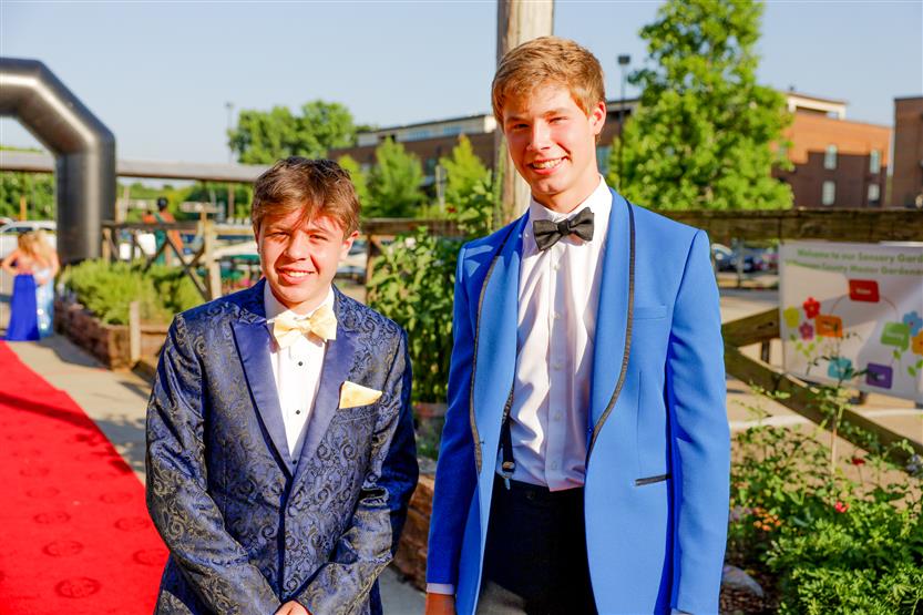 Two young men wearing suits stand on the red carpet